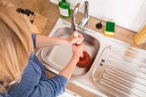 Woman in need of affordable drain cleaning services plunging a drain