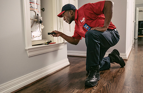 A Mr. Rooter Plumbing professional using a flashlight to inspect a broken water heater