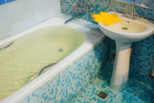Flooded bathtub in blue-tiled bathroom in need of plumbers in Dayton, OH.