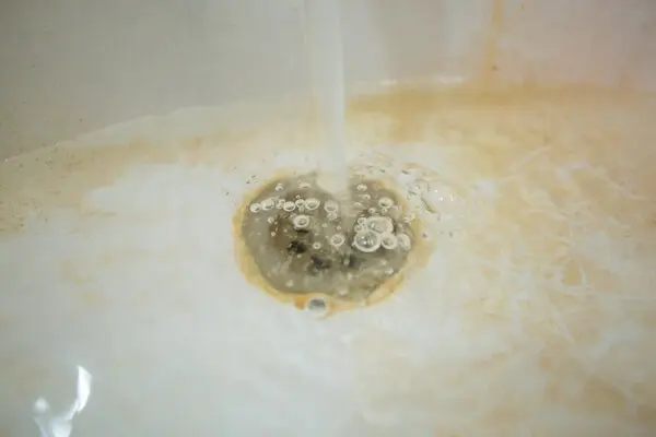 Close-up of drain in clogged tub with yellow stains.