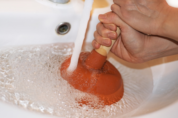 Woman using plunger to clear clog in sink, with water running