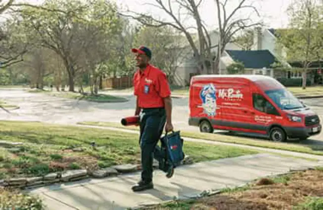 A Mr. Rooter plumber walking up to a house in a residential neighborhood.