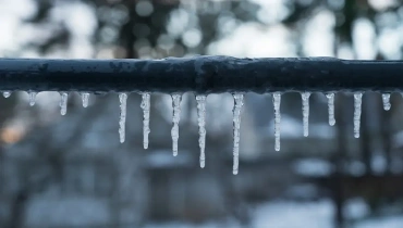 Several icicles of different lengths hang from a gray exterior pipe.