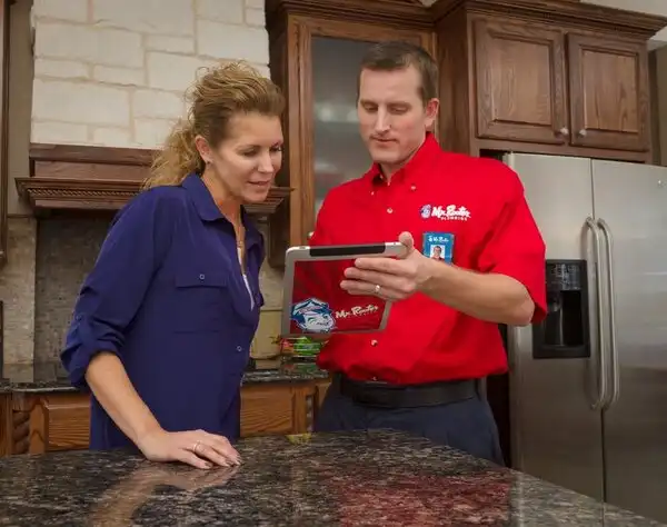 Mr. Rooter plumber showing customer something on a Mr. Rooter tablet while standing in customer's kitchen.