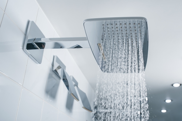 Water coming from a square shower head in modern bathroom with white tile