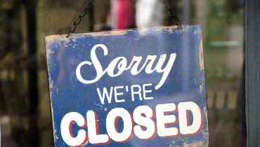 A blue sign reads Sorry, We're Closed in the glass window of a business