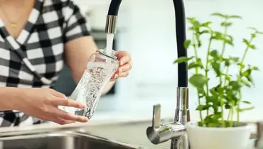 Woman in background pours water from the sink to the reusable bottle | Mr. Rooter Plumbing of Memphis
