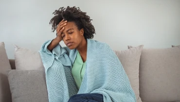 Woman feeling sick at home wrapped in a blanket