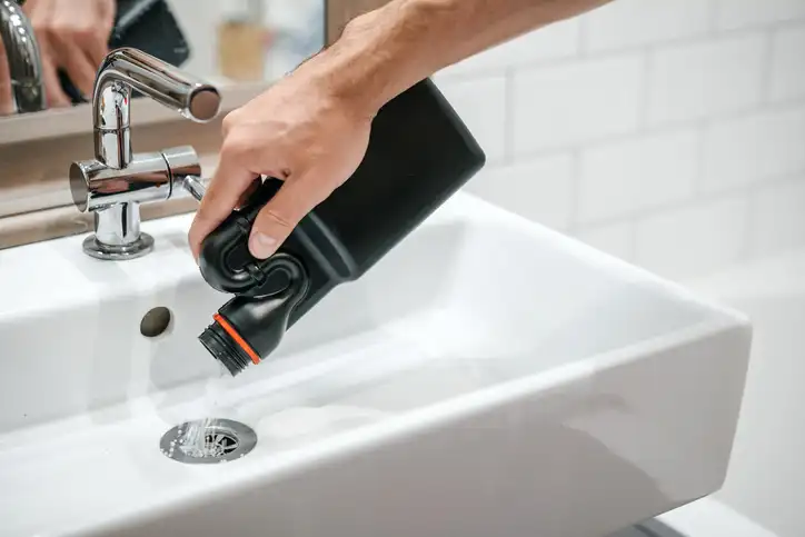 A hand pouring chemical drainer down a drain.