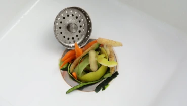 A sink drain clogged with vegetable scraps and in need of garbage disposal repair.