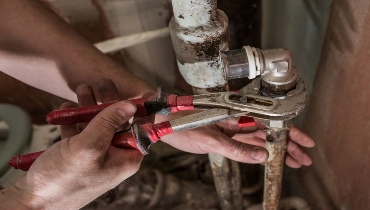 A person uses a wrench on an old, corroded pipe