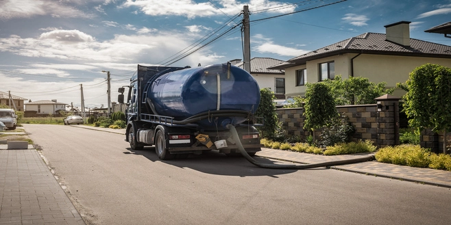 A sewage truck sits parked in front of a suburban row of homes pumping a septic tank system.