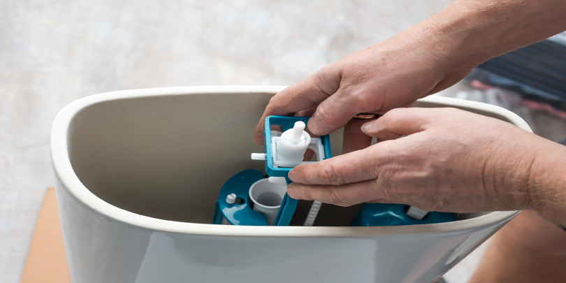 A plumber repairs a water pump in a ceramic toilet cistern.