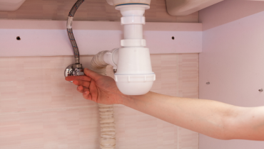 A hand is shown turning the shut-off valve under a white sink.