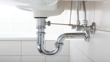Exposed silver plumbing under a bathroom sink.