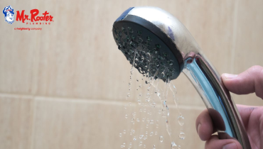 A hand holding a stainless steel shower head with water trickling out of it.