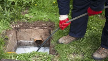 Plumber with ground sewer cover open, unblocking an underground line problem with a tool