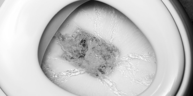 A close view of a running toilet’s basin as water flows down through its drain.
