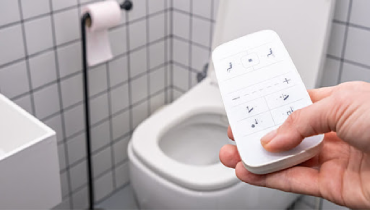 Hand pointing a bidet remote at a toilet