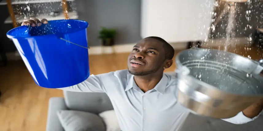 African American Man Holding Buckets Under Leaking Ceiling