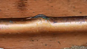 A close-up of a broken copper pipe with a crack in a side of the pipe where it has split open.