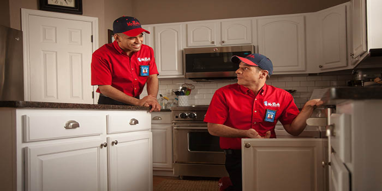 Two Mr. Rooter plumbers working in kitchen