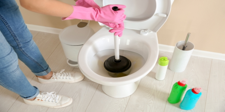 Woman wearing pink rubber gloves using a plunger to unclog a toilet
