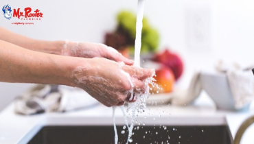 Hands rinsing off under stream of water in a kitchen sink, with vegetables on the countertop in the background.