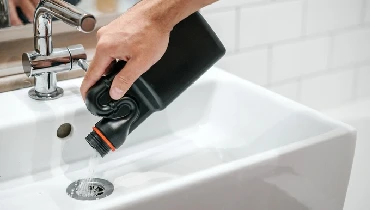 A man pours a chemical drain cleaner into a white porcelain sink with a silver faucet.