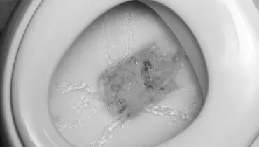A close-up of a toilet bowl with water running down the sides and into the drain below.
