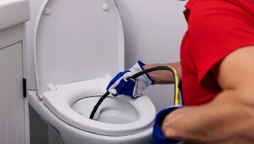 plumber unclogging blocked toilet with hydro jetting at home bathroom.
