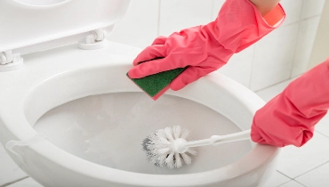 A pair of hands wearing protective gloves cleaning a toilet bowl with a sponge and a scrubber. | Mr. Rooter Plumbing of Pomona Valley