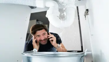 A worried man calls a plumber for help while looking at a leaking pipe under his sink. | Mr. Rooter® Plumbing of Greater Charleston