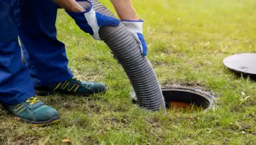 A man inserts a large hose into a septic tank to perform maintenance.