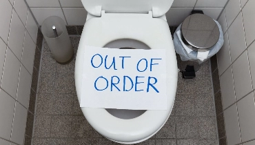 A toilet with out of order sign placed over the seat blocking its use.