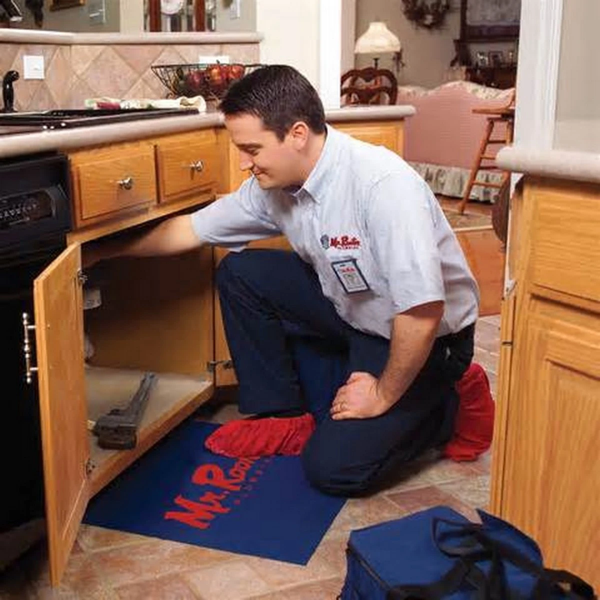 A plumber from Mr. Rooter plumbing inspecting the drain pipes underneath a kitchen sink.