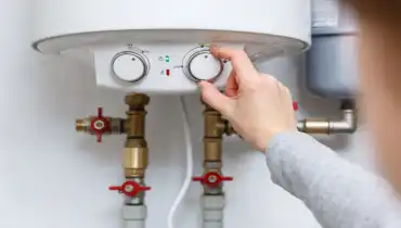 A hand adjusting a tankless water heater, attached to the wall to be out of the way