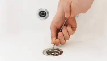 Plumber using a drain snake to unclog the bath's drain