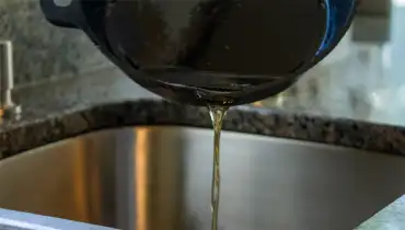 Oil being poured from a cast-iron pan into a stainless steel sink.