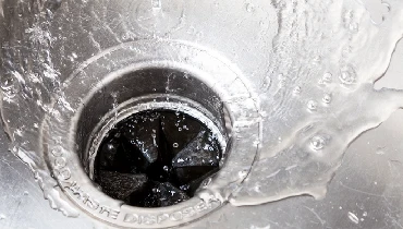 Water flows into a garbage disposal in a stainless steel sink.