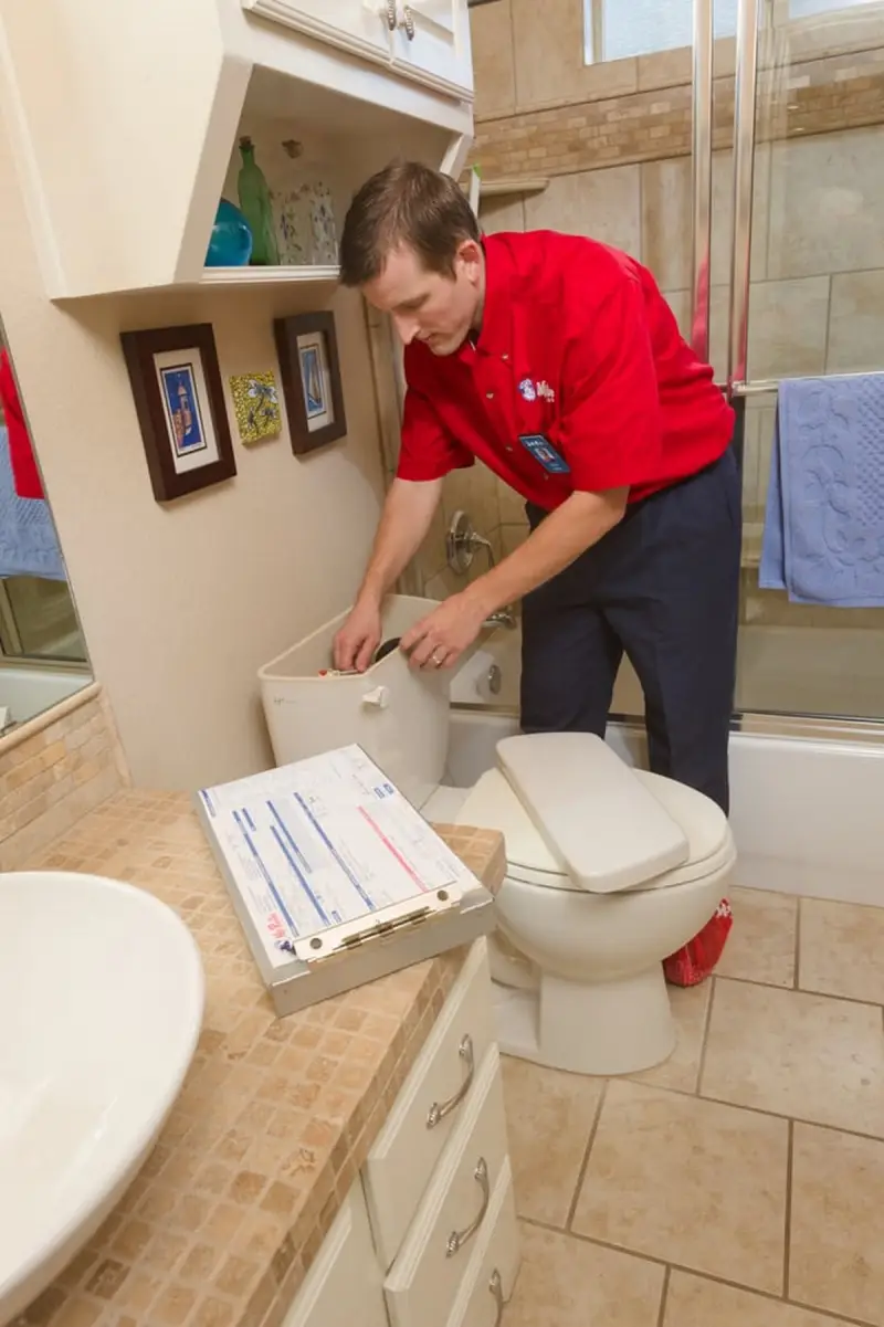 A plumber from Mr. Rooter plumbing inspecting the inside of a toilet tank.