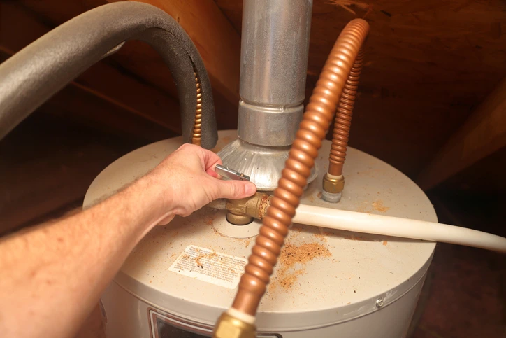 Hand testing the temperature and pressure relief valve on a home water heater during annual plumbing maintenance.