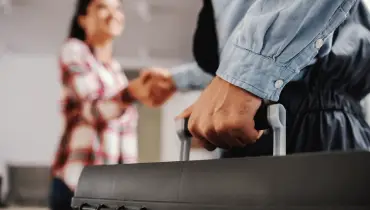 Close-up of a hand gripping a tool case while two people shake hands in the background.