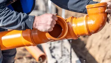 Close-up of hands fitting orange PVC sewer pipes in a trench.