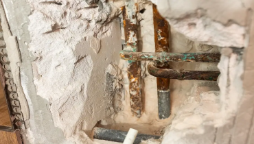 Rusty, corroded pipes exposed through a broken wall for access to a slab foundation leak repair.