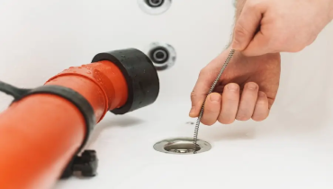 Homeowner using a drain snake to clear a clogged bathtub, with the drain snake inserted into the tub's drain opening.