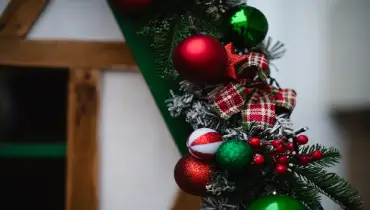 A detailed view of a Christmas garland decorated with red and white ornaments, plaid ribbons, pinecones, and berries