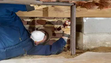 Plumber ​​inspecting pipe insulation of water line in a residential crawl space.