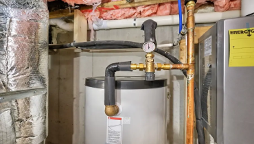 Thermostatic mixing valve installed on copper piping above a residential water heater in a basement.