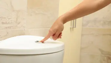 A woman pressing the dual flush button on the top of a bathroom toilet.
